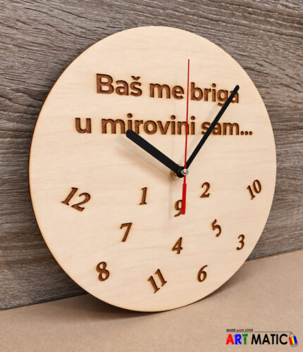 Drveni zidni sat s graviranim natpisom „Baš me briga u mirovini sam” i razbacanim brojevima na drvenoj pozadini.